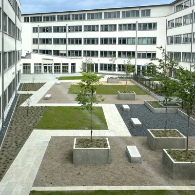 Das Foto zeigt den begrünten Innenhof eines Bürogebäudes mit Pflanzbeeten, Wegen und Sitzmöglichkeiten.