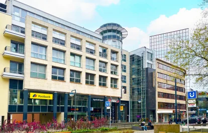 Das Bild zeigt die Frontansicht des Westfalenforums Dortmund mit Geschäften, Postbank, Fitnessstudio und moderner Glasarchitektur.