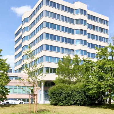 Bürohochhaus mit heller Fassade, umgeben von Grünflächen und altem Baumbestand