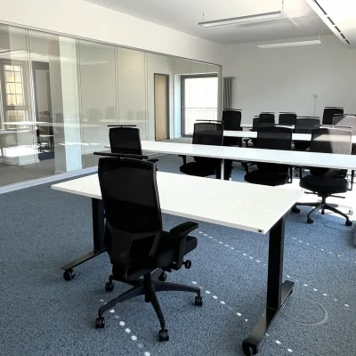 In einem modernen Großraumbüro in Frankfurt stehen mehrere Schreibtische mit ergonomischen Stühlen und Blick auf große Fenster.