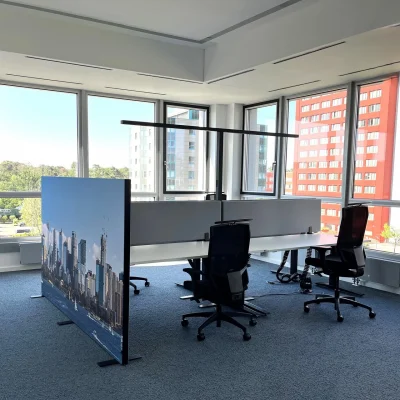 Ein Arbeitsplatz im Großraumbüro in Frankfurt mit moderner Ausstattung, Trennwand und Ausblick auf umliegende Bürogebäude.