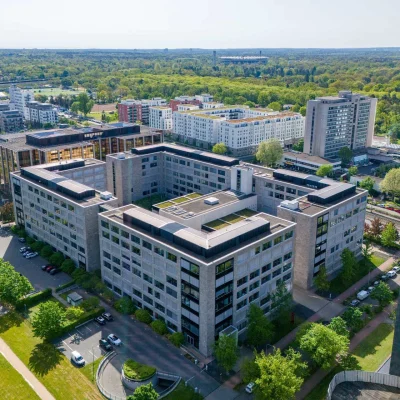 Die Luftaufnahme zeigt ein modernes Bürogebäude im Frankfurter Stadtteil Niederrad mit umliegenden Grünflächen und Nachbargebäuden.