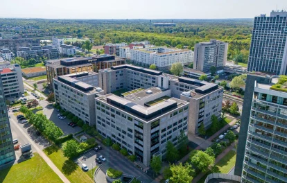 Die Luftaufnahme zeigt ein modernes Bürogebäude im Frankfurter Stadtteil Niederrad mit umliegenden Grünflächen und Nachbargebäuden.