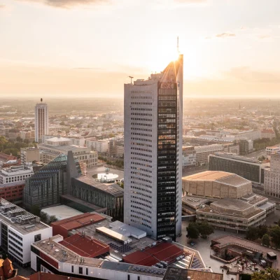 Nahaufnahme des City-Hochhauses Leipzig mit EEX-Logo bei Sonnenaufgang über der Stadt.