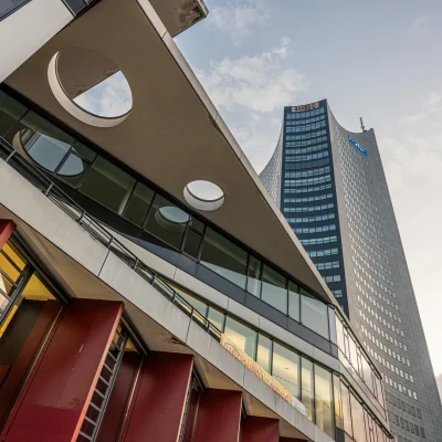 Blick nach oben entlang der Glasfassade des City-Hochhauses Leipzig zwischen zwei modernen Gebäuden.