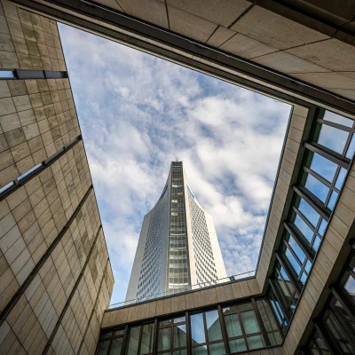 Das City-Hochhaus Leipzig ist aus der Froschperspektive zwischen modernen Gebäuden zu sehen.