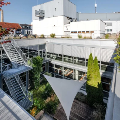 Ein moderner Büro-Innenhof mit Terrasse, Glasfassade, Metalltreppe und umliegender Stadtbebauung.