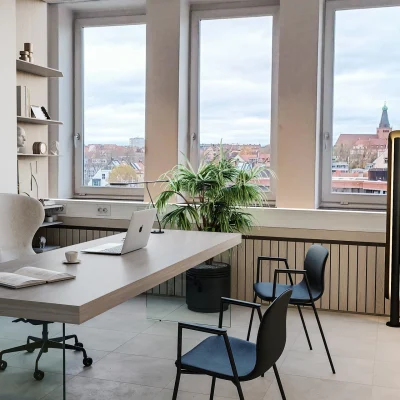 Ein modern eingerichtetes Büro mit großem Schreibtisch, Ausblick auf die Stadt und einer Pflanze am Fenster.