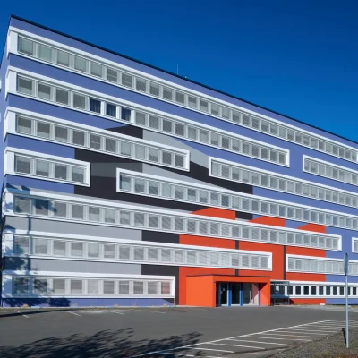 Außenansicht eines modernen Bürogebäudes mit auffälliger Fassadengestaltung und Parkplätzen.