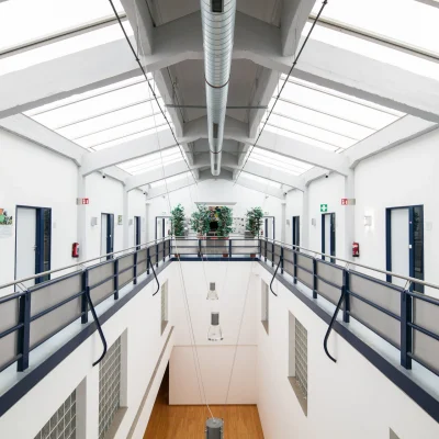 Leerer Innenbereich einer großen Halle mit Oberlichtern und sichtbaren Versorgungsleitungen.