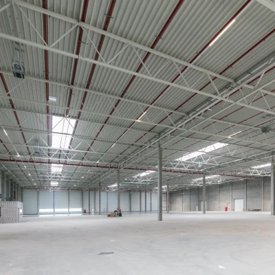 Innenansicht einer großen, leeren Industriehalle mit sichtbarem Stahltragewerk und mehreren Rolltoren.