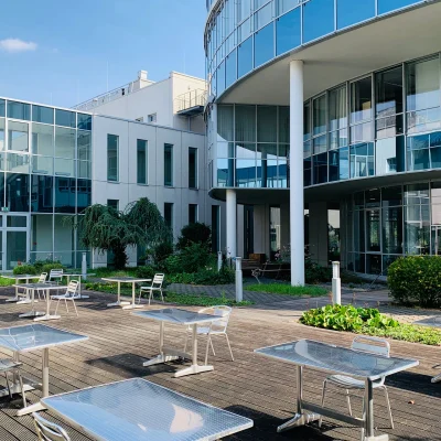 Moderner Innenhof eines Bürogebäudes mit Glasfassade und möblierter Terrasse als Pausen- oder Arbeitsbereich.