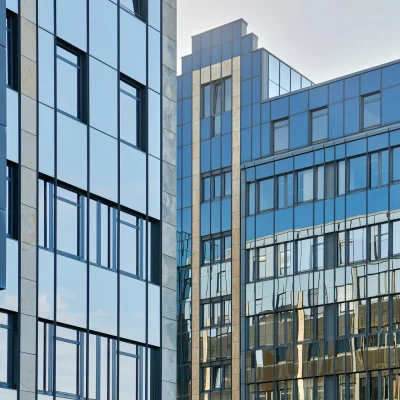 Eine moderne Glasfassade eines Bürohochhauses mit Spiegelung des Himmels und umliegender Gebäude.