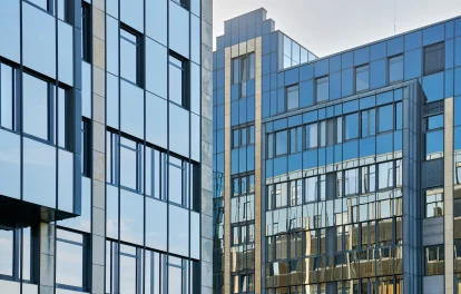 Eine moderne Glasfassade eines Bürohochhauses mit Spiegelung des Himmels und umliegender Gebäude.
