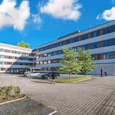 Das Bild zeigt die moderne Außenansicht eines Bürogebäudes mit Parkplätzen in Frankfurt.