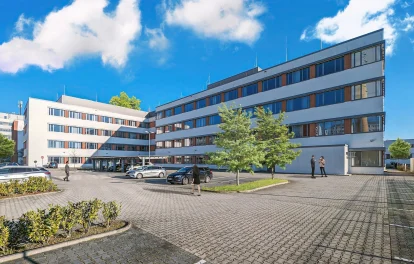 Das Bild zeigt die moderne Außenansicht eines Bürogebäudes mit Parkplätzen in Frankfurt.
