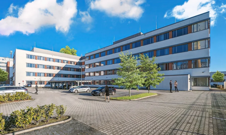 Das Bild zeigt die moderne Außenansicht eines Bürogebäudes mit Parkplätzen in Frankfurt.