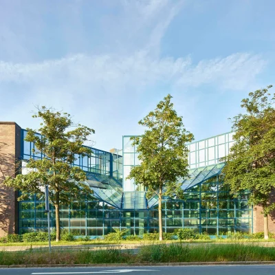 Moderne Glasfassade eines Bürokomplexes mit symmetrischer Architektur und Baumbestand.