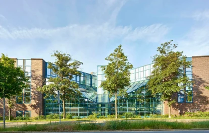 Moderne Glasfassade eines Bürokomplexes mit symmetrischer Architektur und Baumbestand.