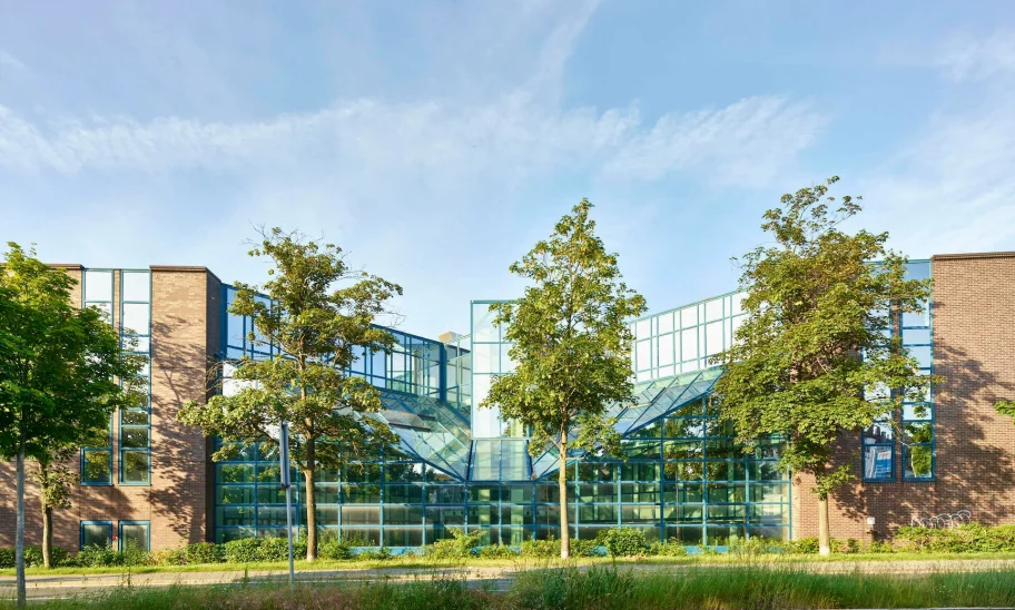 Moderne Glasfassade eines Bürokomplexes mit symmetrischer Architektur und Baumbestand.