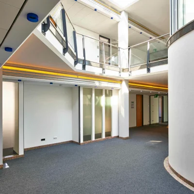 Offener Empfangsbereich mit Galerie, Glasbrüstung und Lichtleiste in einem modernen Bürogebäude.
