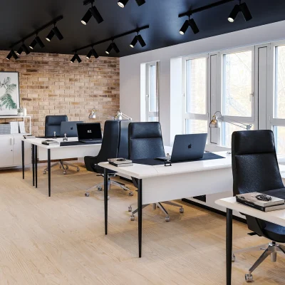 Mehrere moderne Arbeitsplätze mit Computern und ergonomischen Stühlen in einem hellen Büroraum mit großen Fenstern und Regal.