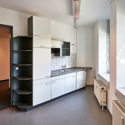 Kleine Teeküche mit Küchenzeile, Spülbecken und Fenster in einem Bürogebäude.