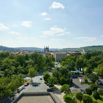 Weitläufiger Ausblick über die Stadt Würzburg mit grünen Bäumen und typischen Stadtsilhouetten im Hintergrund.