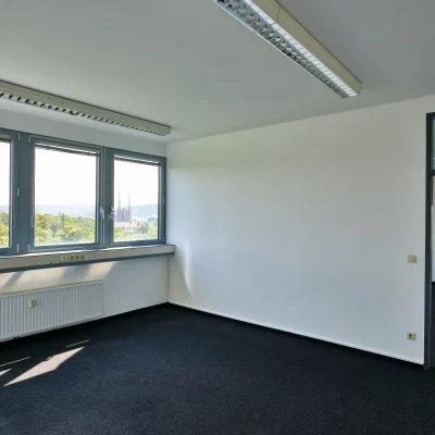 Ein leerer Büroraum mit Teppichboden und mehreren Fenstern mit Ausblick auf das Stadtgebiet.