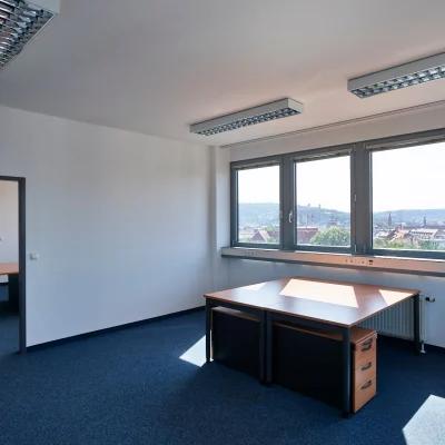 Büroraum mit Durchgang zu einem weiteren Raum und großen Fenstern mit Stadtblick.