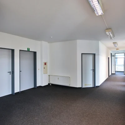 Langer, geräumiger Büroflur mit mehreren Türen und Teppichboden in einem modernen Bürogebäude.
