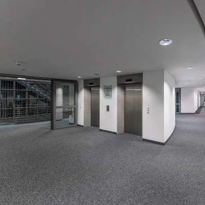 Das Bild zeigt den modernen Flur eines Bürogebäudes in Frankfurt mit zwei Aufzügen und Blick auf den Gebäudekern.