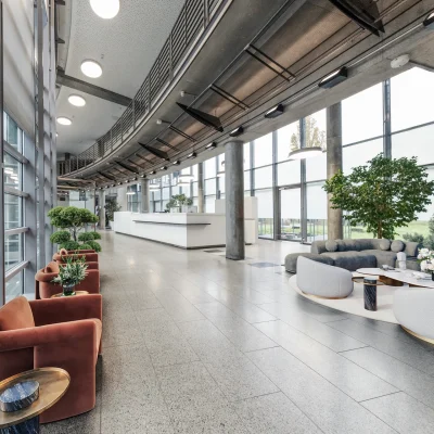 Der Eingangsbereich eines modernen Bürogebäudes in Frankfurt mit Glasfassade, Loungepflanzen und bequemen Sitzmöbeln.