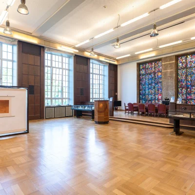 Das Bild zeigt einen Ausstellungsbereich mit Vitrinen und einer kunstvollen Fensterfront.
