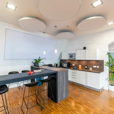 Das Bild zeigt eine moderne Büroküche mit Theke, Kaffeemaschine und Barhockern auf Holzboden.