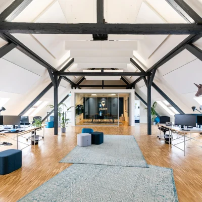 Das Bild zeigt ein modernes Büroloft mit Holzboden, offenen Arbeitsplätzen und sichtbaren Dachschrägen.
