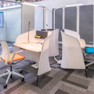 Moderne Einzelarbeitsplätze mit ergonomischen Stühlen und Schreibtischen in einem gläsernen Büro mit Teppichboden.