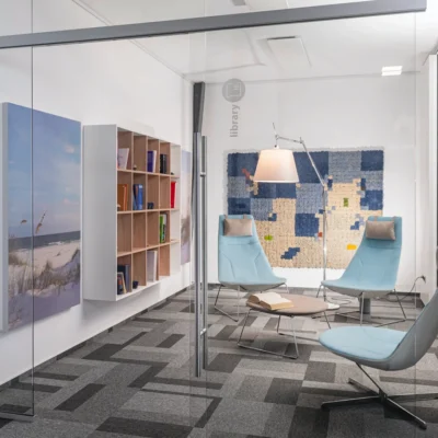 Kleiner Besprechungsraum oder Rückzugsbereich mit Sesseln, Bücherregal und Wandkunst in einem modernen Büro.