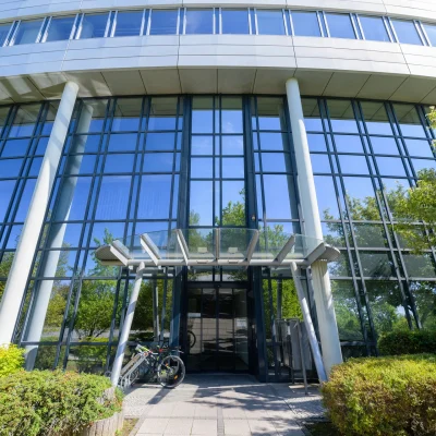 Der Eingangsbereich eines Bürogebäudes in Schwalbach mit großflächiger Glasfassade, Säulen und Fahrradständern.
