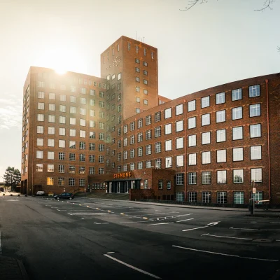 Außenansicht des Werkhaus Siemensdamm von der Straße aus mit der Sonne im Hintergrund