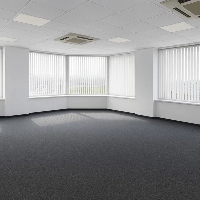 Ein leerer, heller Büroraum mit großen Fenstern, Teppichboden und Klimageräten an der Decke.