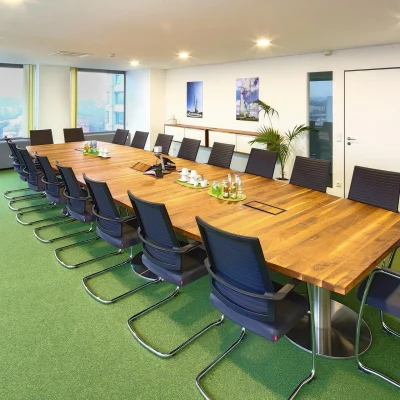 Ein moderner Konferenzraum mit langem Holztisch, bequemen Besucherstühlen und Ausblick durch große Fenster.