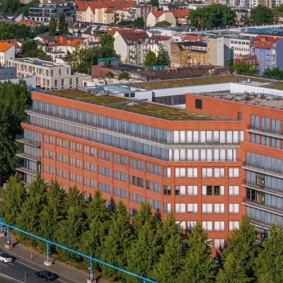 Luftaufnahme eines modernen Bürogebäudes in Berlin mit roter Backsteinfassade und begrüntem Dach.