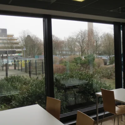 Innenansicht eines Aufenthaltsbereichs im Bürogebäude Adickesallee in Frankfurt mit großen Fensterfronten und Blick ins Grüne sowie angrenzende Außenflächen.