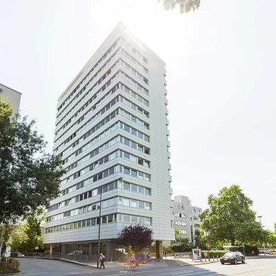 Moderne Außenansicht eines Bürohochhauses an der Adickesallee in Frankfurt mit klarer Fassadenstruktur, reflektierenden Fensterbändern und Sonneneinfall im oberen Gebäudebereich.