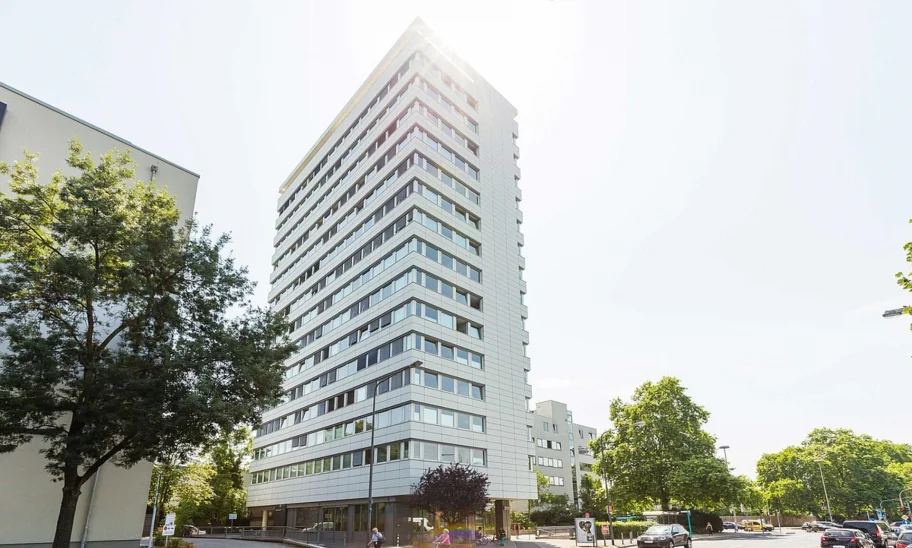 Moderne Außenansicht eines Bürohochhauses an der Adickesallee in Frankfurt mit klarer Fassadenstruktur, reflektierenden Fensterbändern und Sonneneinfall im oberen Gebäudebereich.