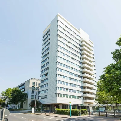 Straßenansicht eines modernen Bürohochhauses in der Adickesallee in Frankfurt mit direkter Anbindung an den öffentlichen Nahverkehr und umgebender städtischer Bebauung.