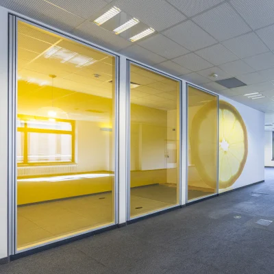 Innenaufnahme einer großzügigen Bürofläche in der Dynamostraße in Mannheim mit gelb getönten Glastrennwänden und einem großen Zitronenmotiv an der Wand; helle, offene Raumgestaltung mit Rasterdecke und großen Fenstern im Hintergrund.