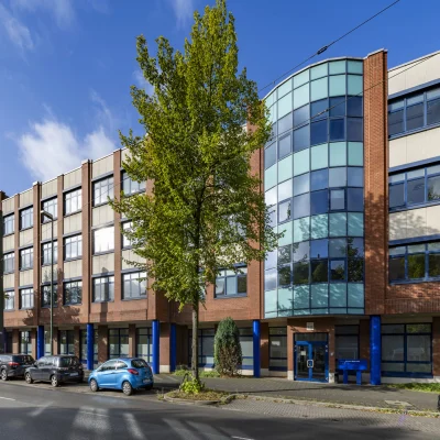 Außenansicht eines mehrgeschossigen Büroensembles an der Erkrather Straße in Düsseldorf mit roter Klinkerfassade, markanten Glasbauteilen und begrüntem Straßenraum.