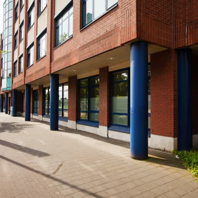 Ansicht des Erdgeschosses eines Bürogebäudes an der Erkrather Straße in Düsseldorf mit Arkadengang, blauen Stützen und großflächigen Fensterfronten entlang des Gehwegs.